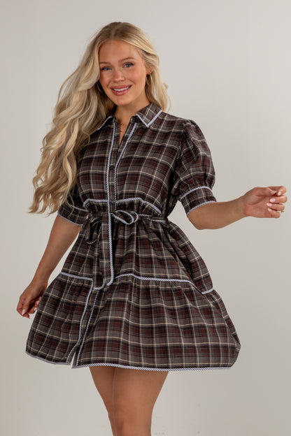 Woman wearing a plaid dress with a belt on a plain background
