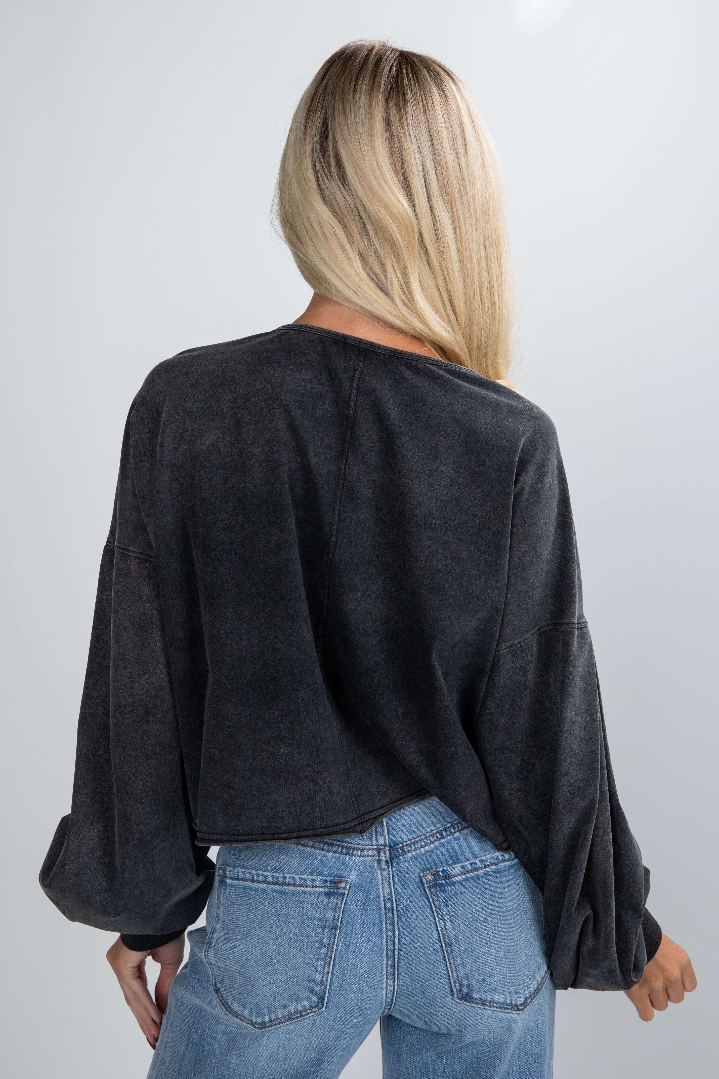 Person wearing a black oversized sweater and blue jeans on a plain background