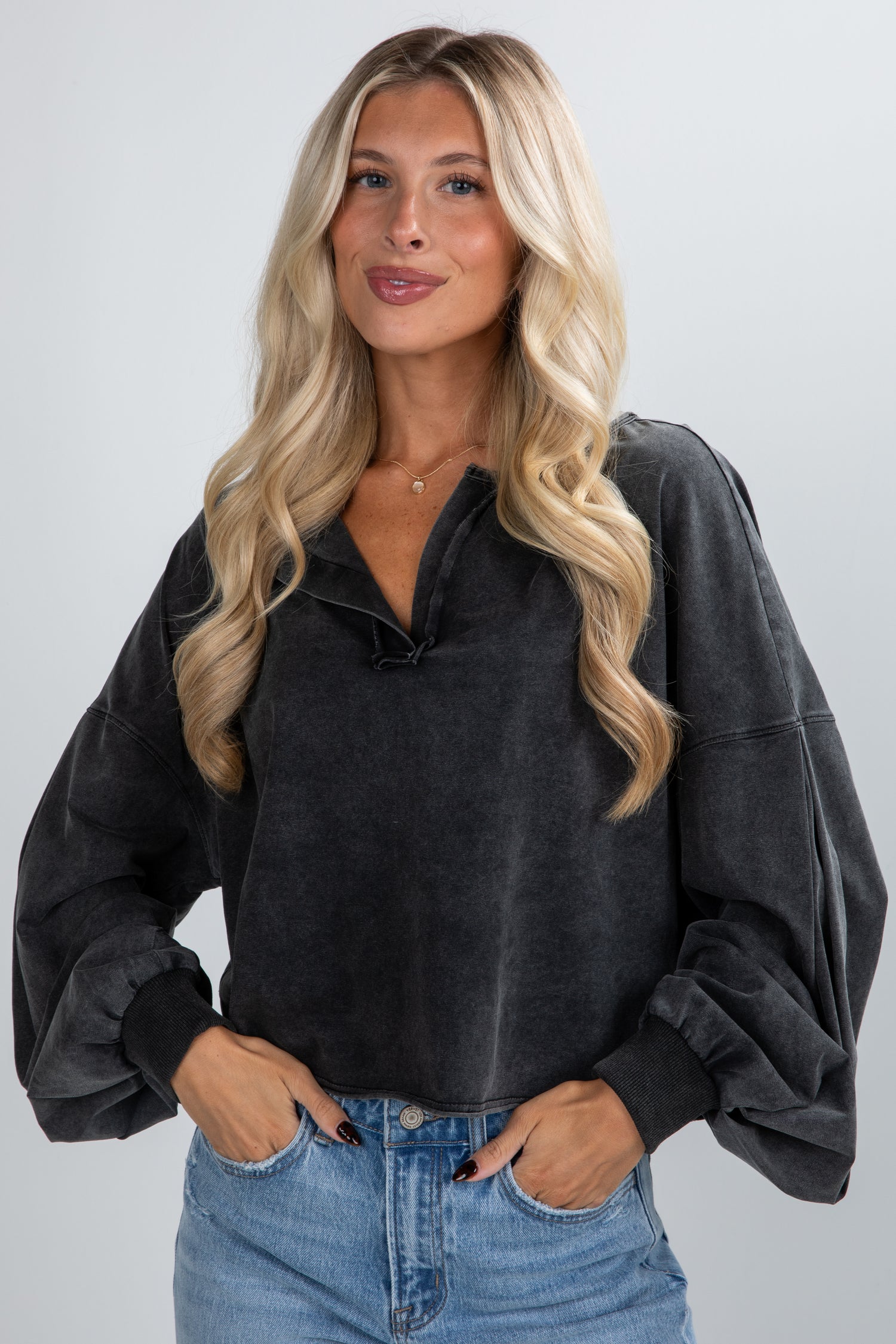 Woman wearing a dark gray oversized sweater and blue jeans against a plain background