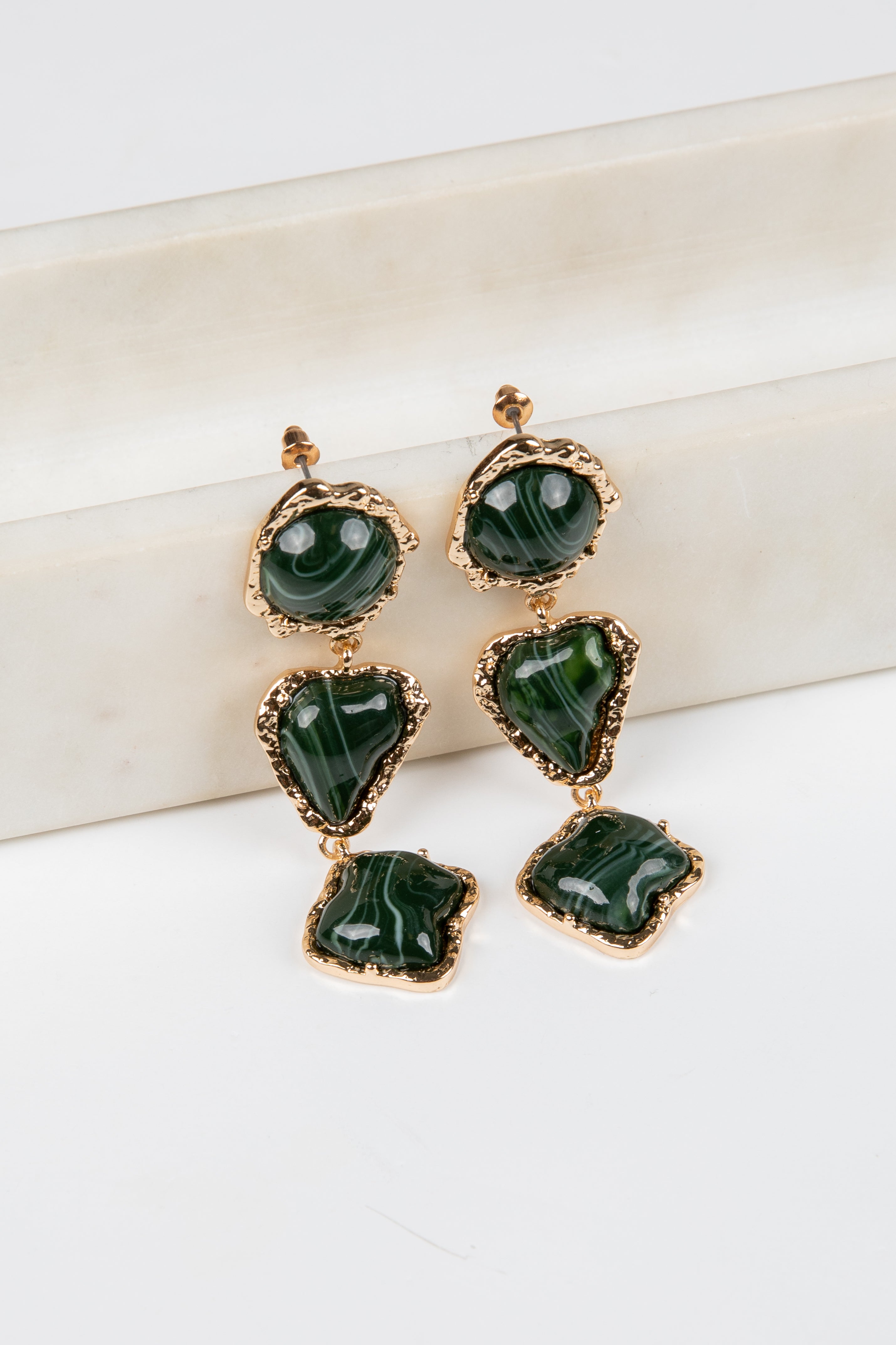 Green earrings with gold accents on a white surface