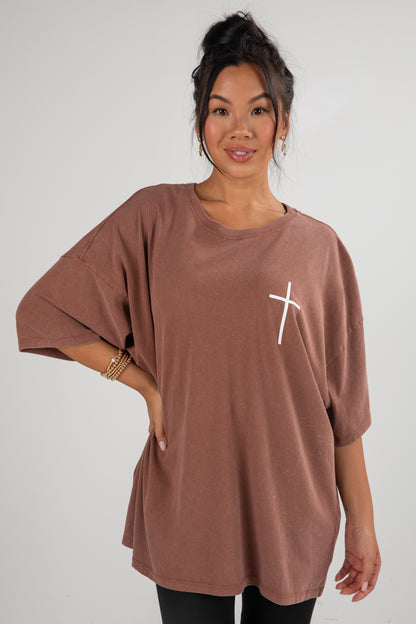 Woman wearing a brown tunic with a white cross design on a plain background