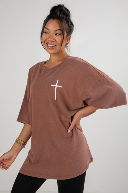 Woman wearing a brown t-shirt with a white cross design on a plain background