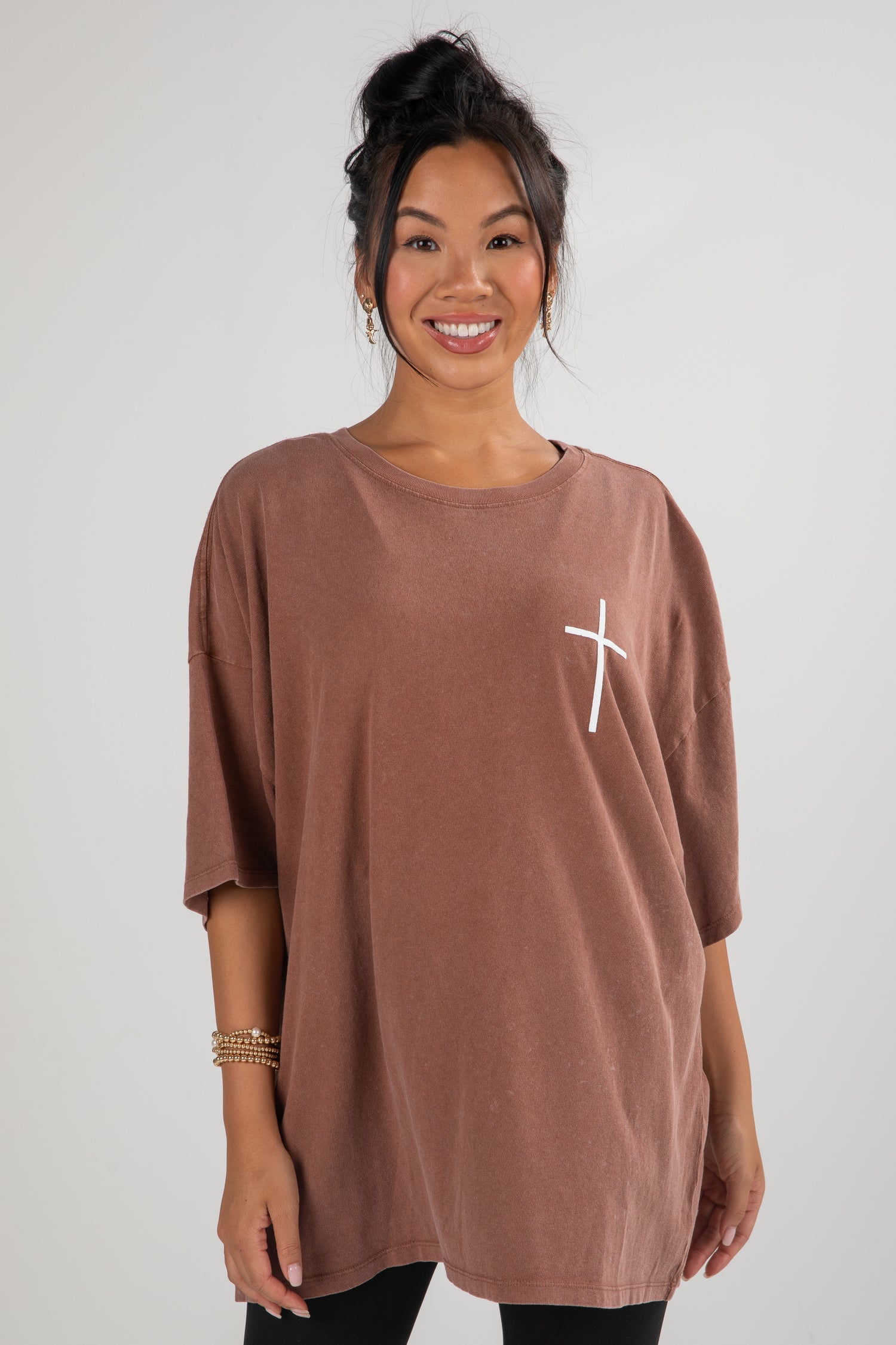 Woman wearing a brown tunic with a white logo on a plain background