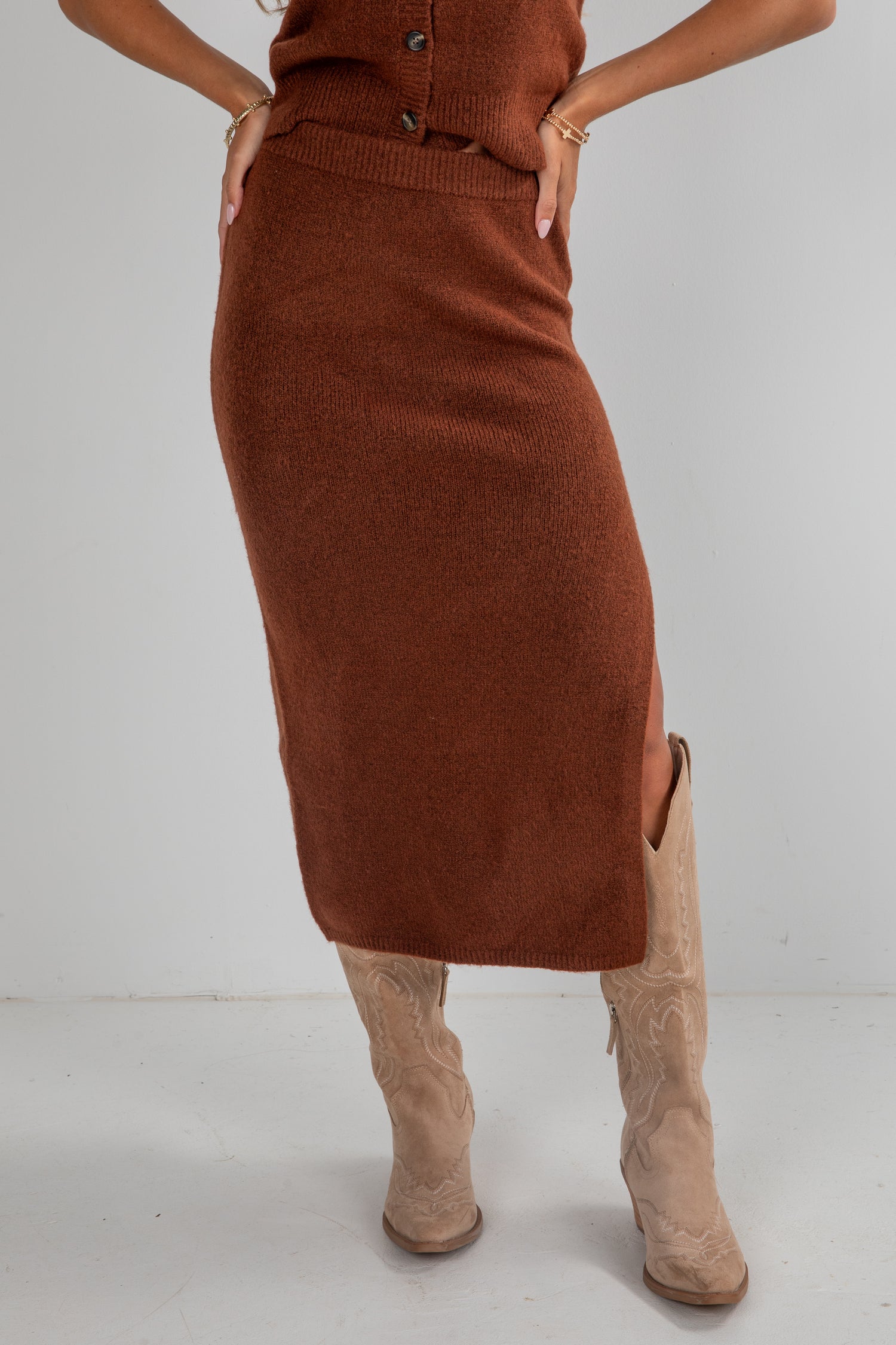 Person wearing a brown knit skirt and beige boots on a white background