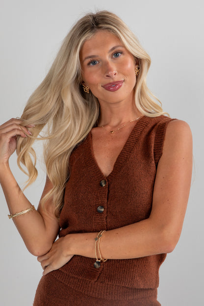 Woman wearing a brown sleeveless cardigan against a plain background