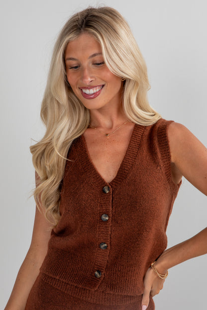 Woman wearing a brown knitted vest against a plain background