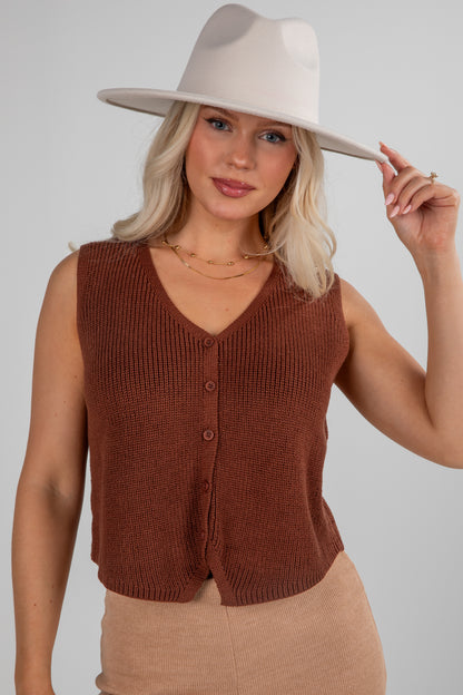 Woman wearing a brown knitted vest and beige hat against a plain background