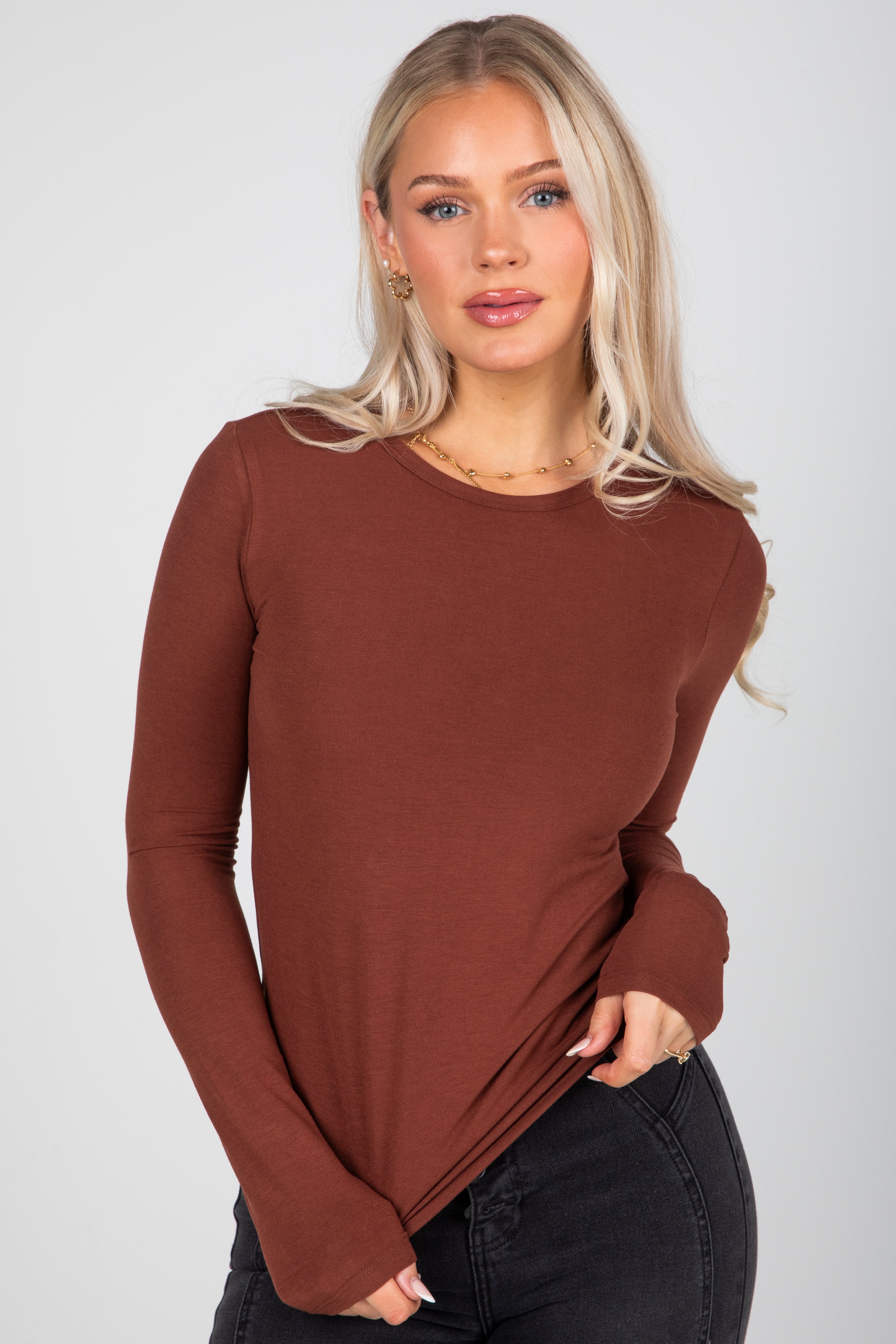 Woman wearing a brown long-sleeve top against a plain background