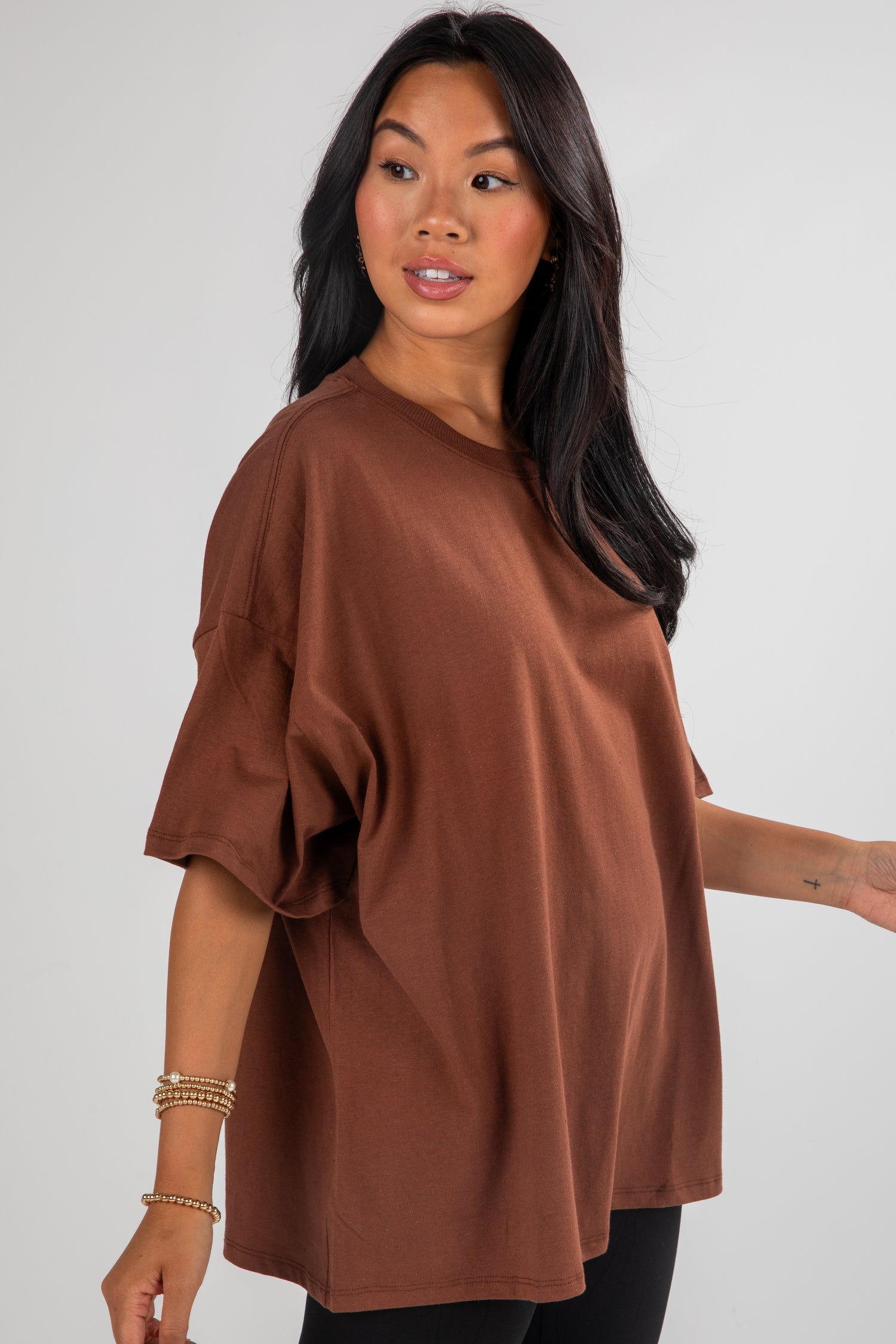 Woman wearing a brown oversized top against a plain background