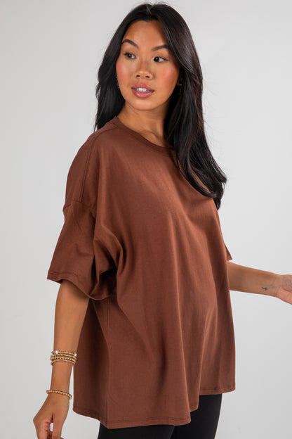 Woman wearing a brown oversized top against a plain background