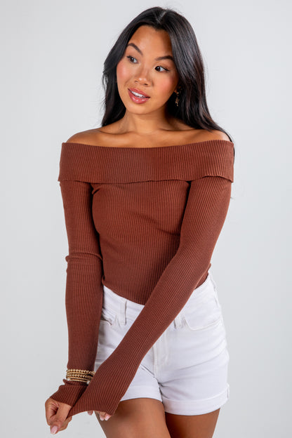 Woman wearing a brown off-shoulder top and white shorts on a plain background