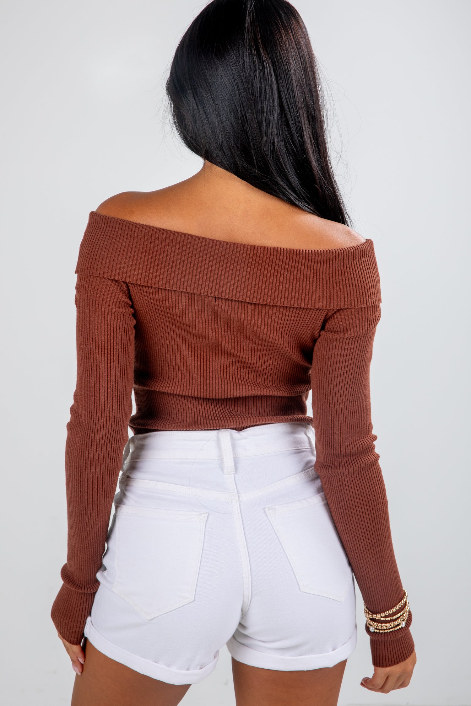 Woman wearing a brown off-shoulder top and white shorts on a plain background