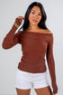 Woman wearing a brown off-shoulder sweater and white shorts on a plain background