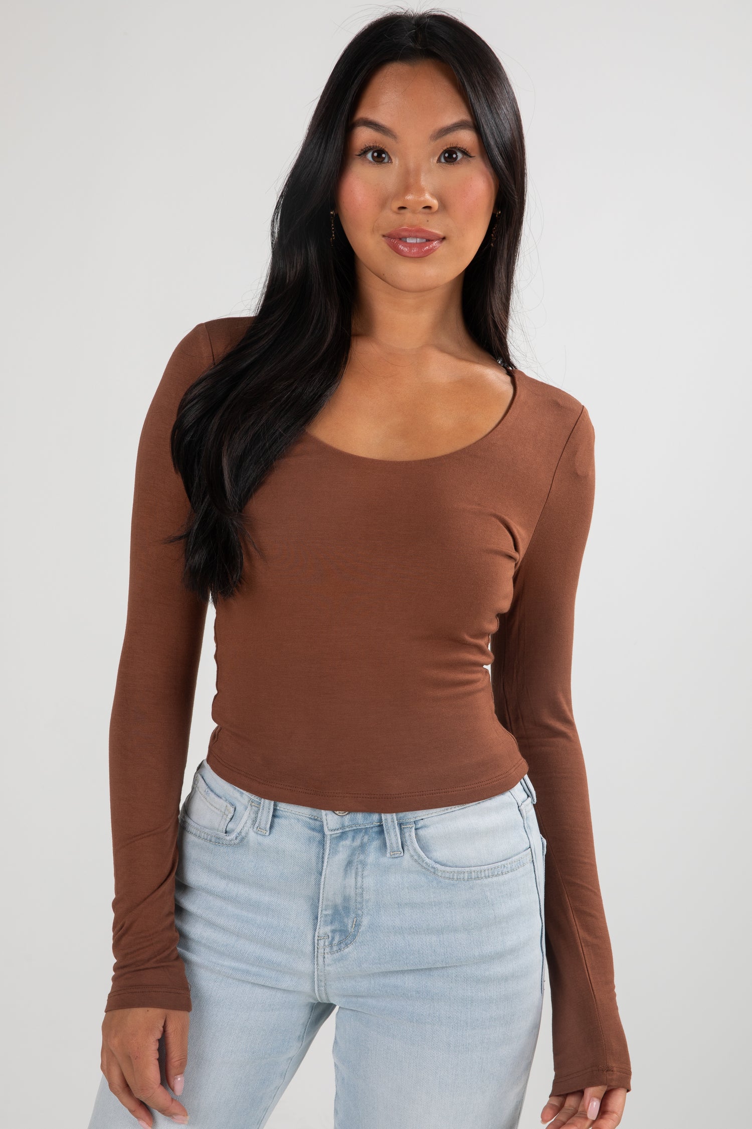 Woman wearing a brown long-sleeve top and light blue jeans against a white background