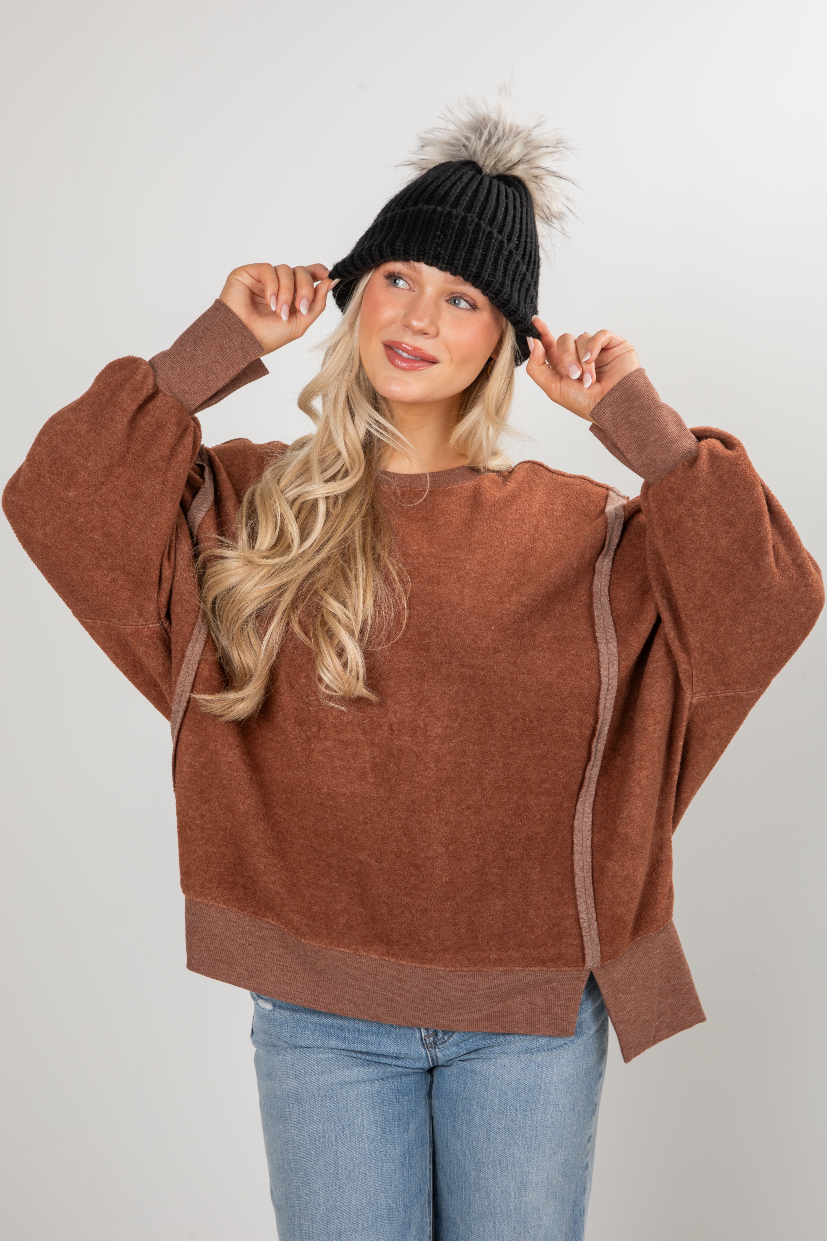 Woman wearing a brown sweater and black beanie with a pom-pom on a white background