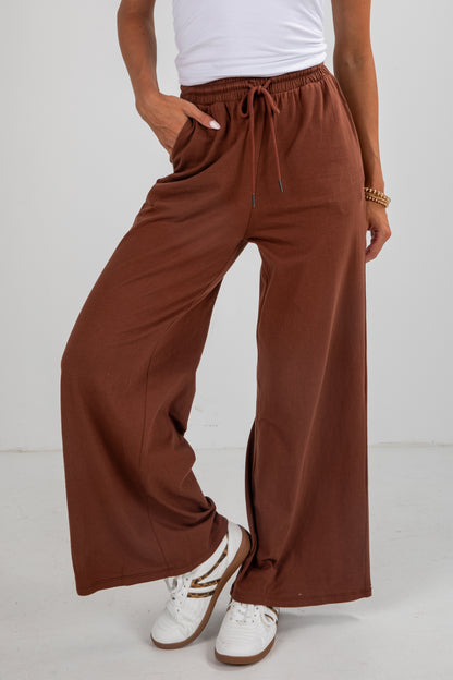 Person wearing brown wide-leg pants and white sneakers on a white background