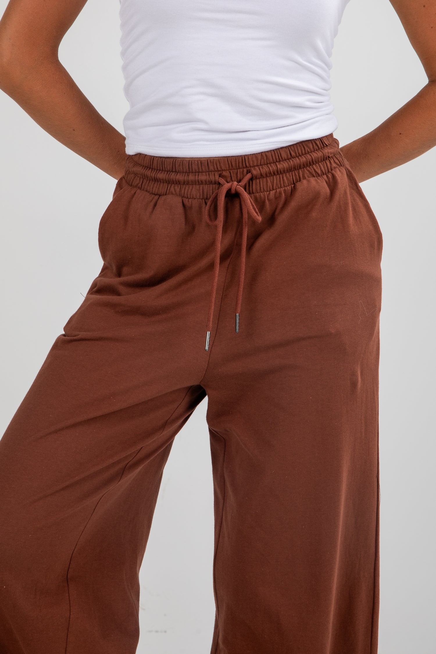 Brown wide-leg pants with a white top on a plain background