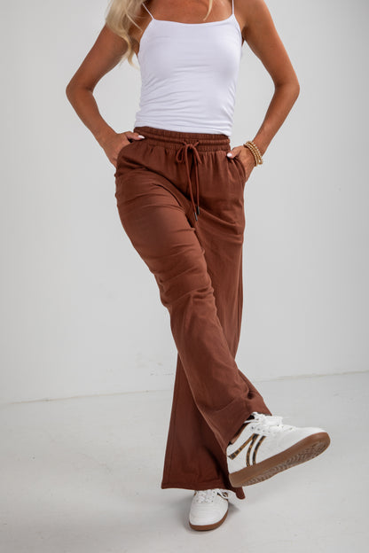 Person wearing brown wide-leg pants and white sneakers on a plain background
