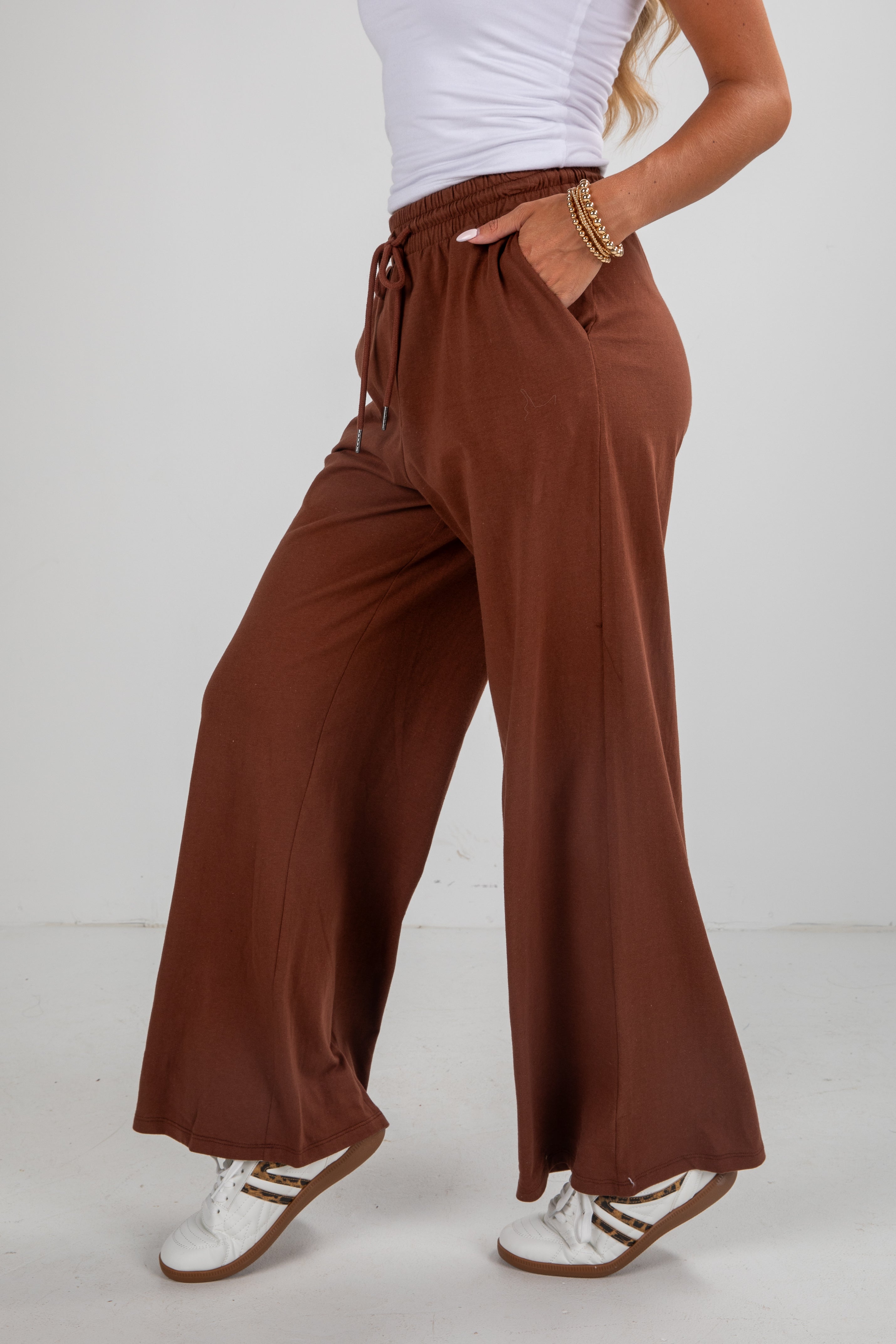 Person wearing brown wide-leg pants and white sneakers on a plain background