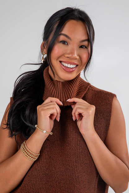 Woman wearing a brown sleeveless sweater against a plain background