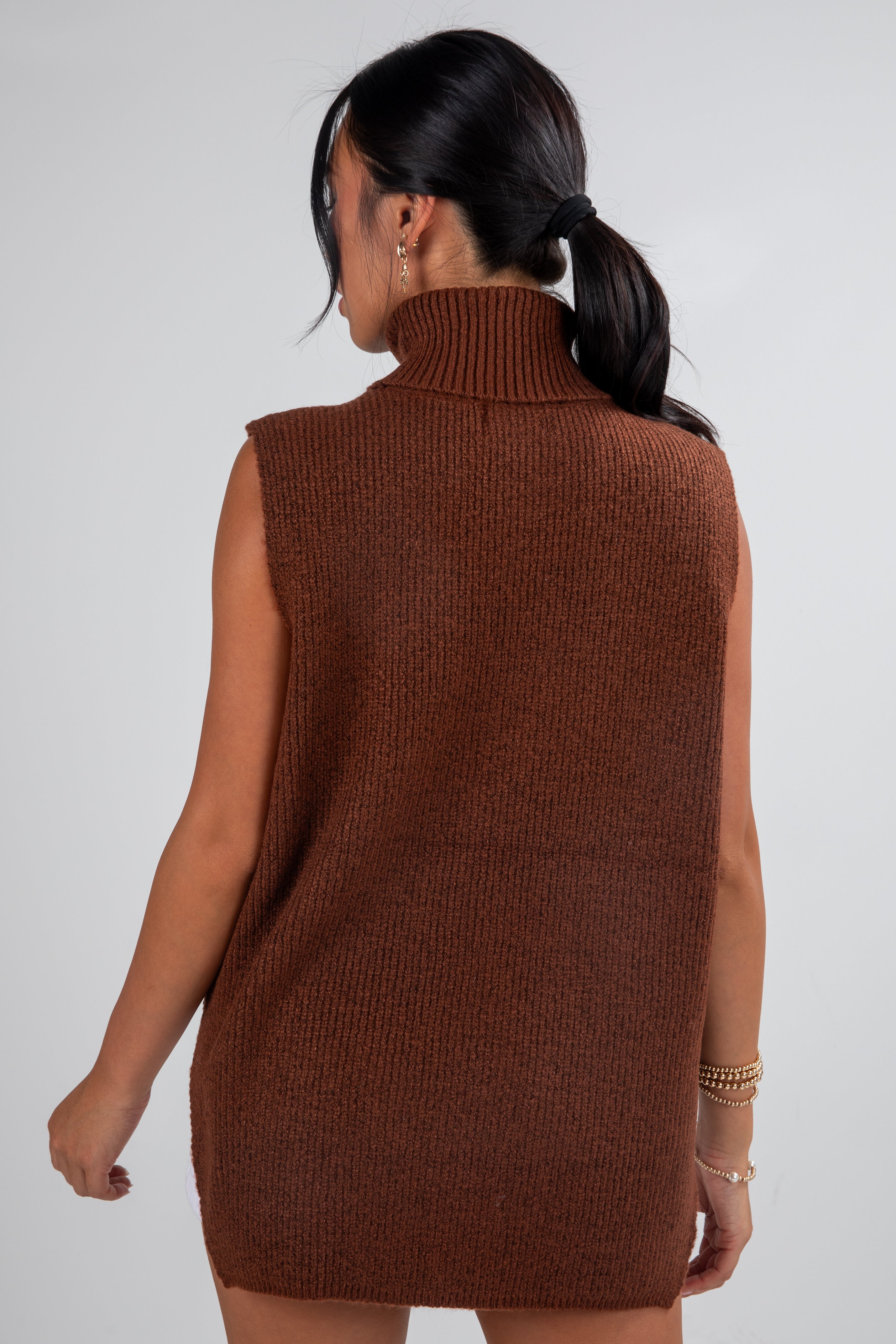 Woman wearing a brown knitted sleeveless dress against a white background