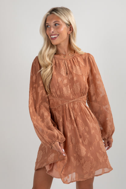 Woman wearing a brown dress with long sleeves against a plain background