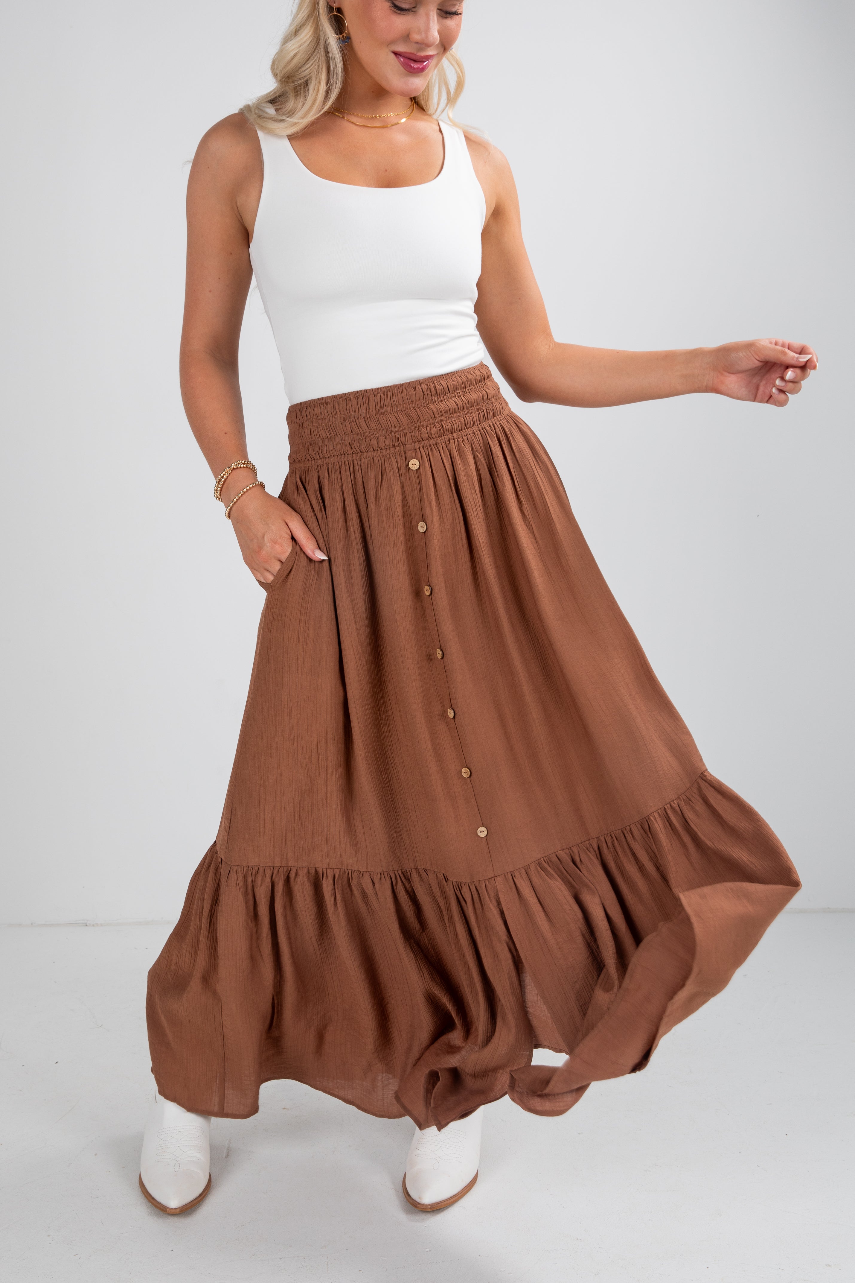 Woman wearing a white tank top and brown maxi skirt on a white background