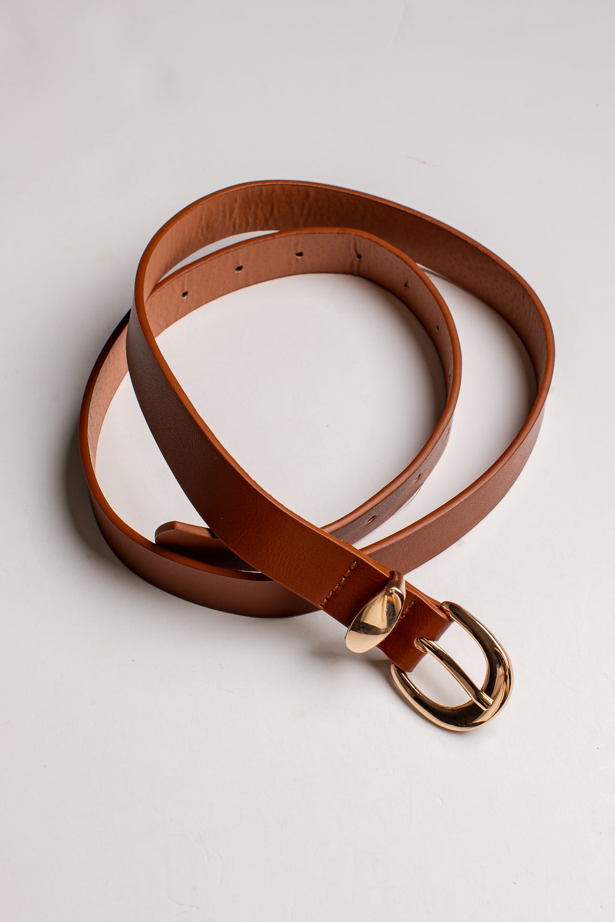 A brown leather belt with a polished gold-tone buckle, coiled on a light gray background.