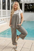Woman in a gray jumpsuit standing by a pool
