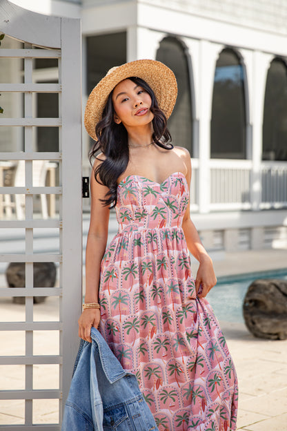 Woman in a pink floral dress and straw hat standing outdoors.
