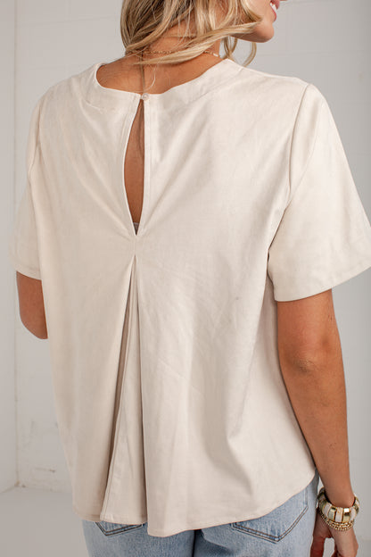 A woman wearing a cream-colored short-sleeve top with a back keyhole cutout, shown from the back against a plain light background.