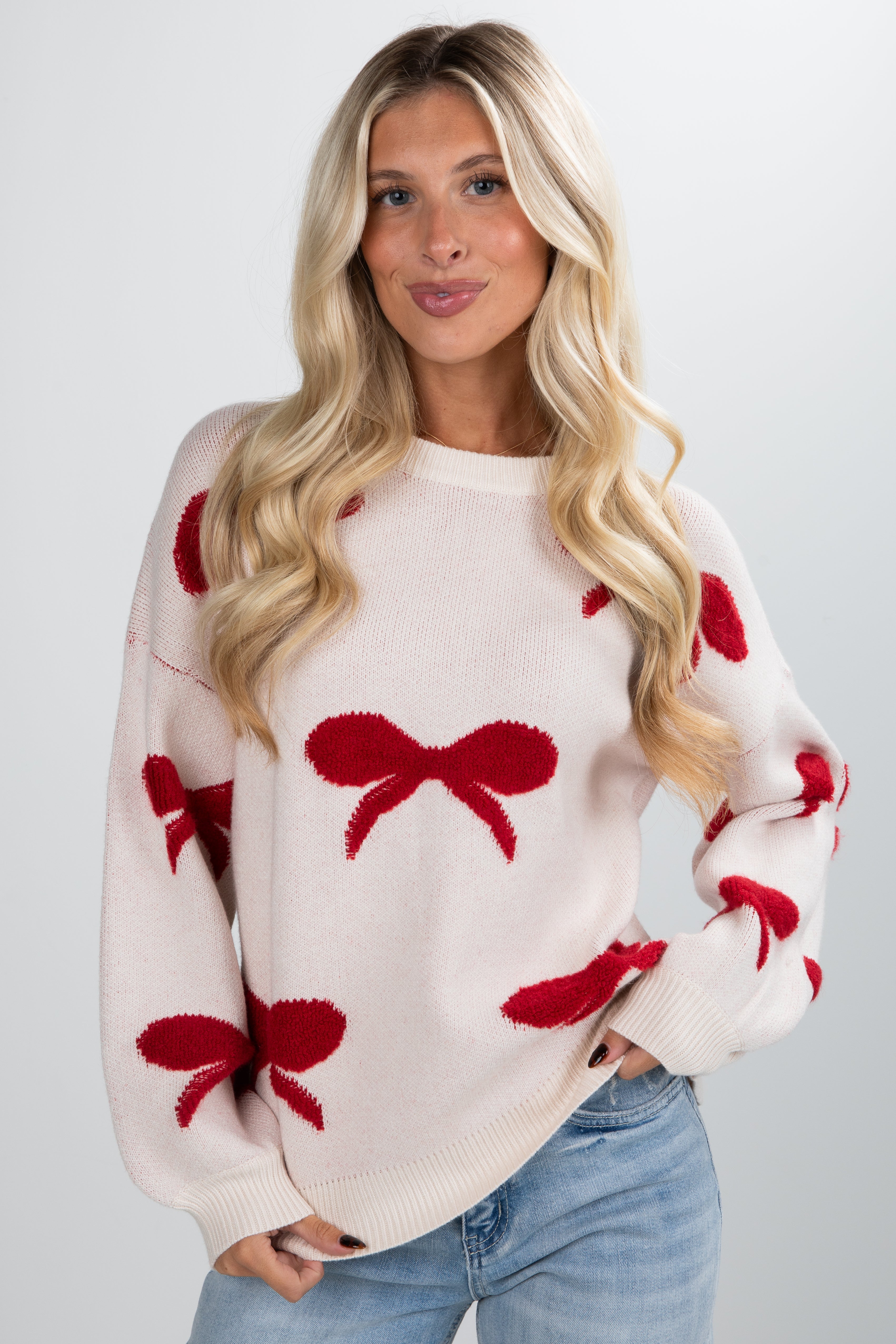 Woman wearing a cream sweater with red bow patterns on a plain background