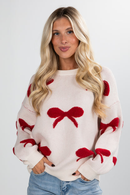 Woman wearing a white sweater with red bow patterns on a plain background