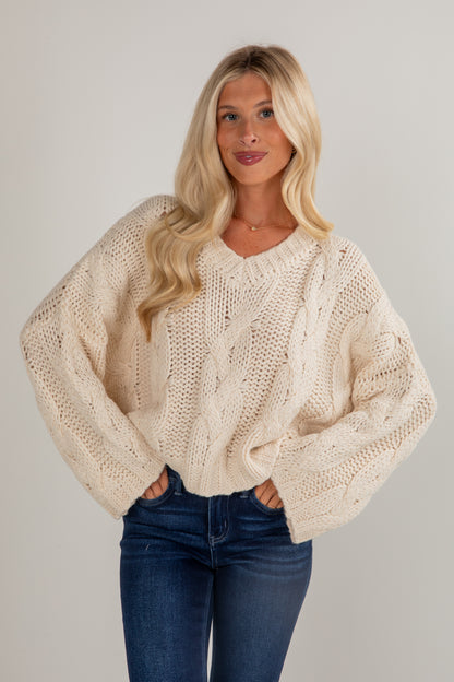 Woman wearing a beige knitted sweater and blue jeans against a plain background