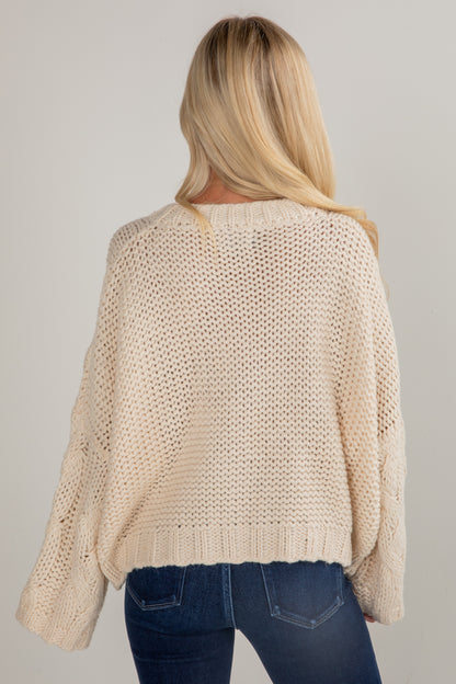 Woman wearing a beige knitted sweater and blue jeans on a plain background