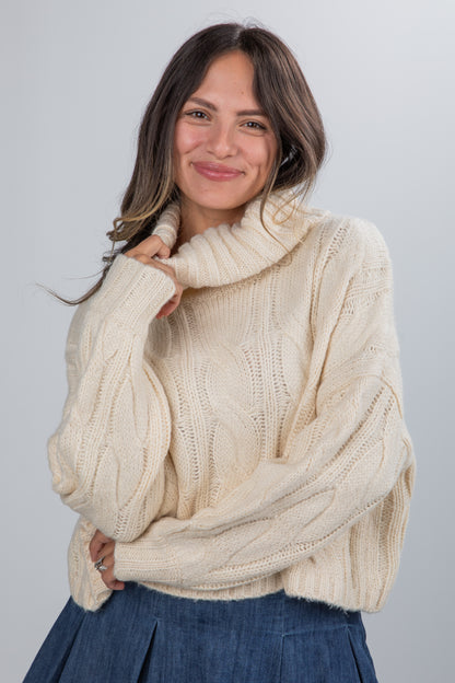 Woman wearing a cream cable knit sweater against a plain background