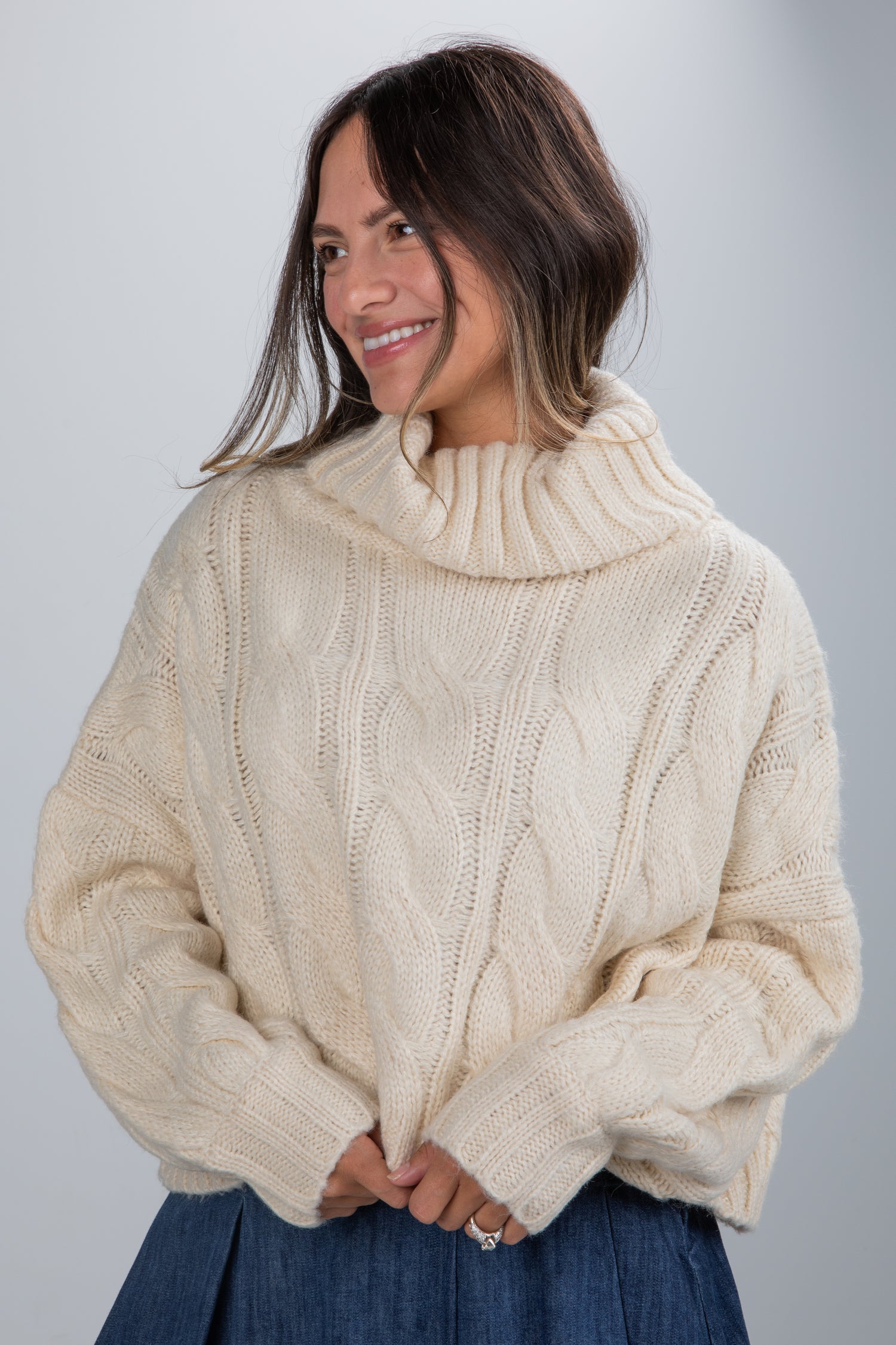 Woman wearing a cream cable knit sweater against a gray background