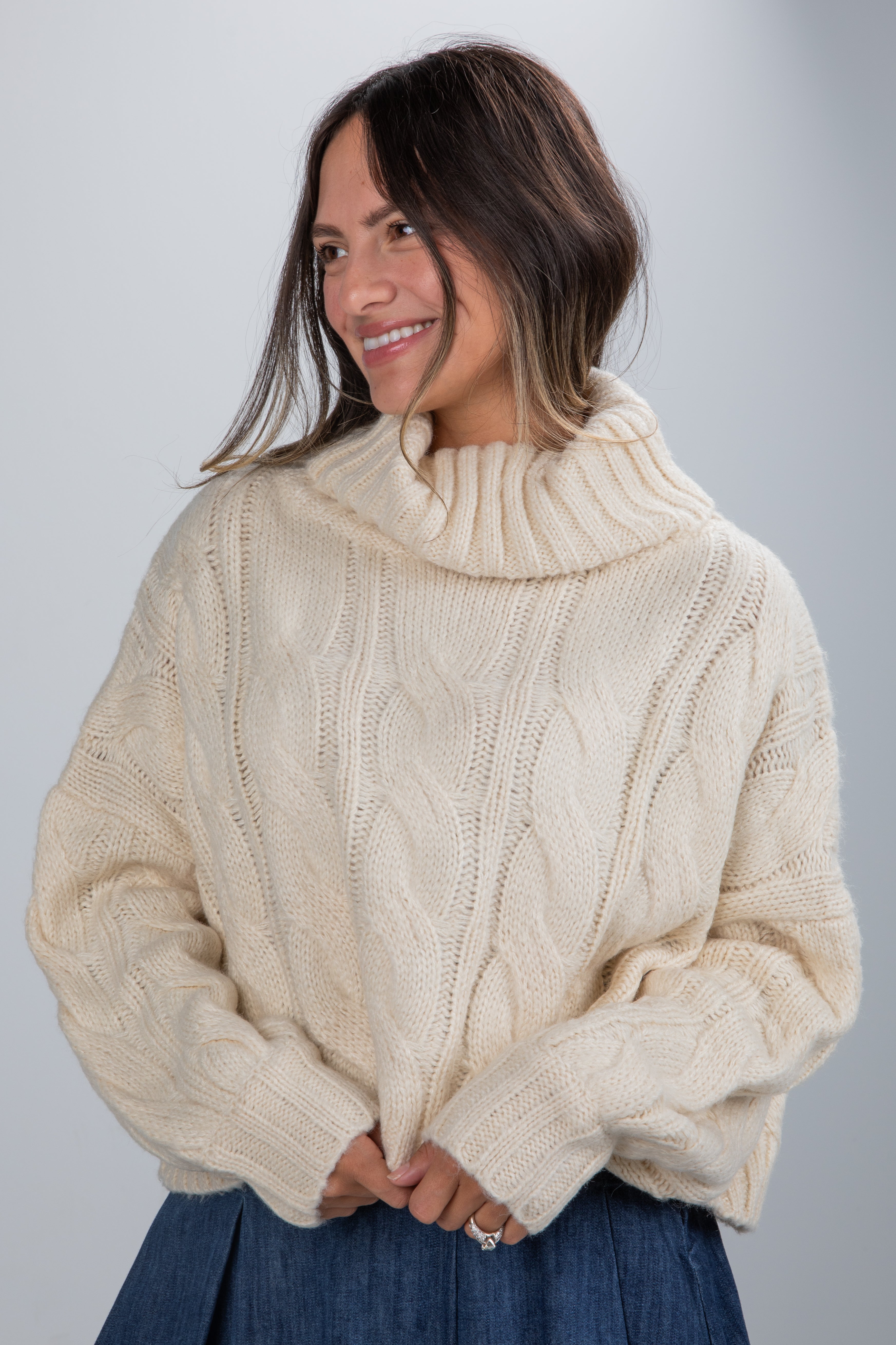 Woman wearing a cream cable knit sweater against a gray background