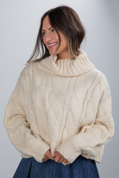 Woman wearing a cream cable knit sweater against a gray background