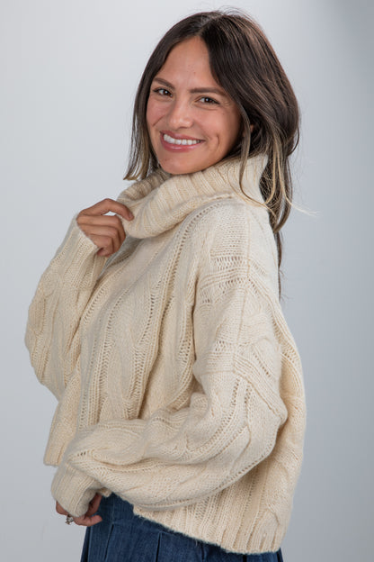 Woman wearing a beige cable knit sweater against a plain background