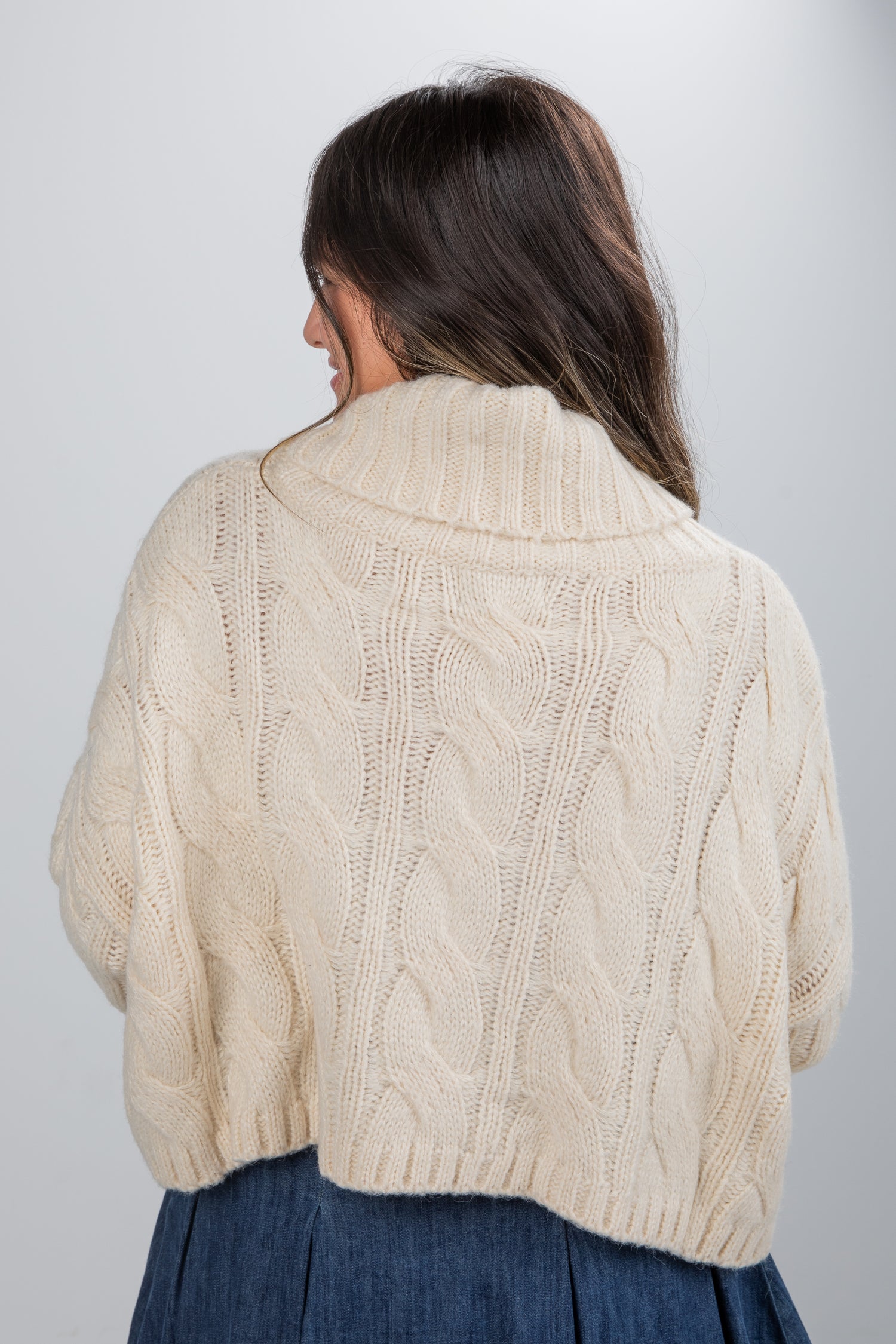 Woman wearing a beige cable knit sweater against a plain background