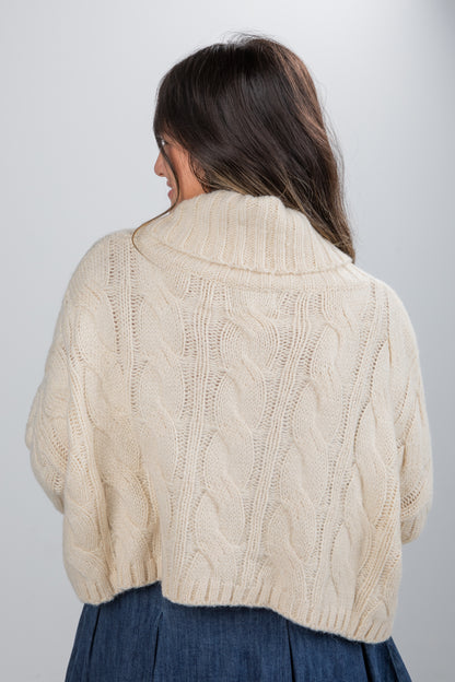 Woman wearing a beige cable knit sweater against a plain background