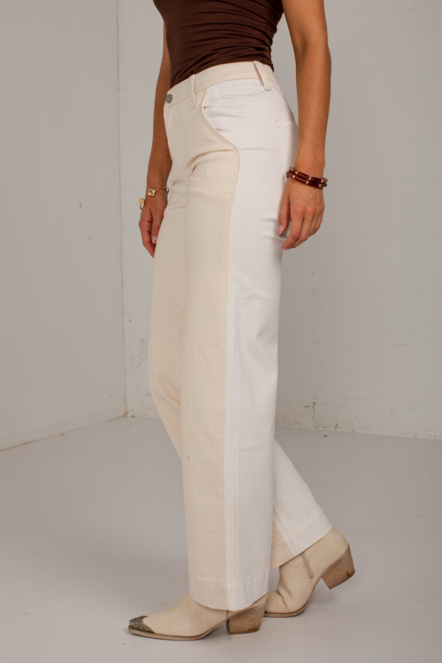 A person wearing off-white wide-leg cropped pants with a brown fitted top and beige heeled boots, standing against a plain light gray wall.