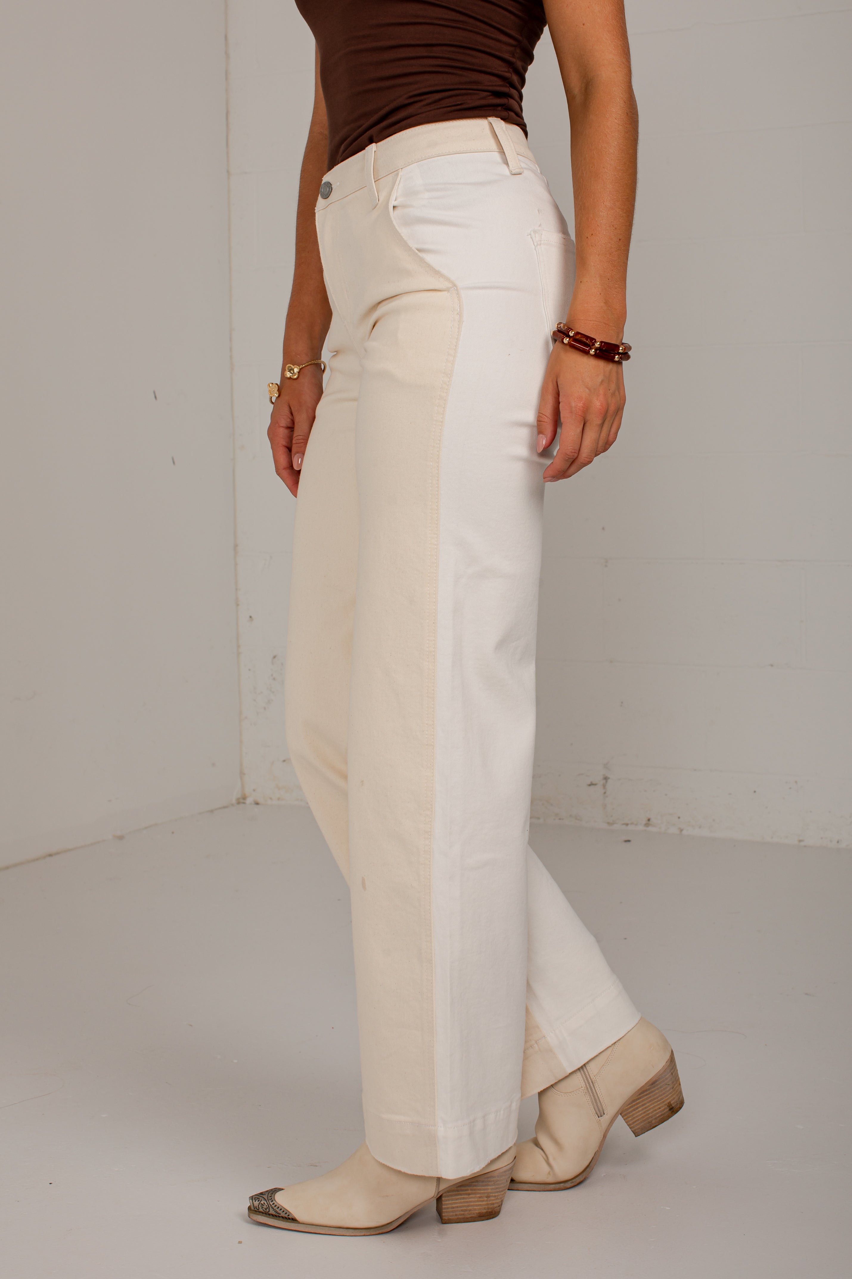A person wearing off-white wide-leg cropped pants with a brown fitted top and beige heeled boots, standing against a plain light gray wall.