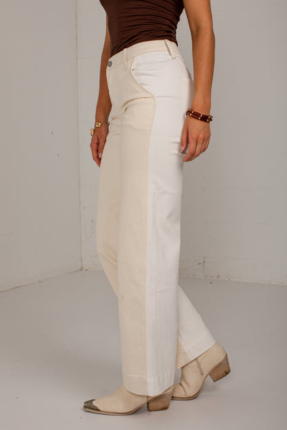 A person wearing off-white wide-leg cropped pants with a brown fitted top and beige heeled boots, standing against a plain light gray wall.