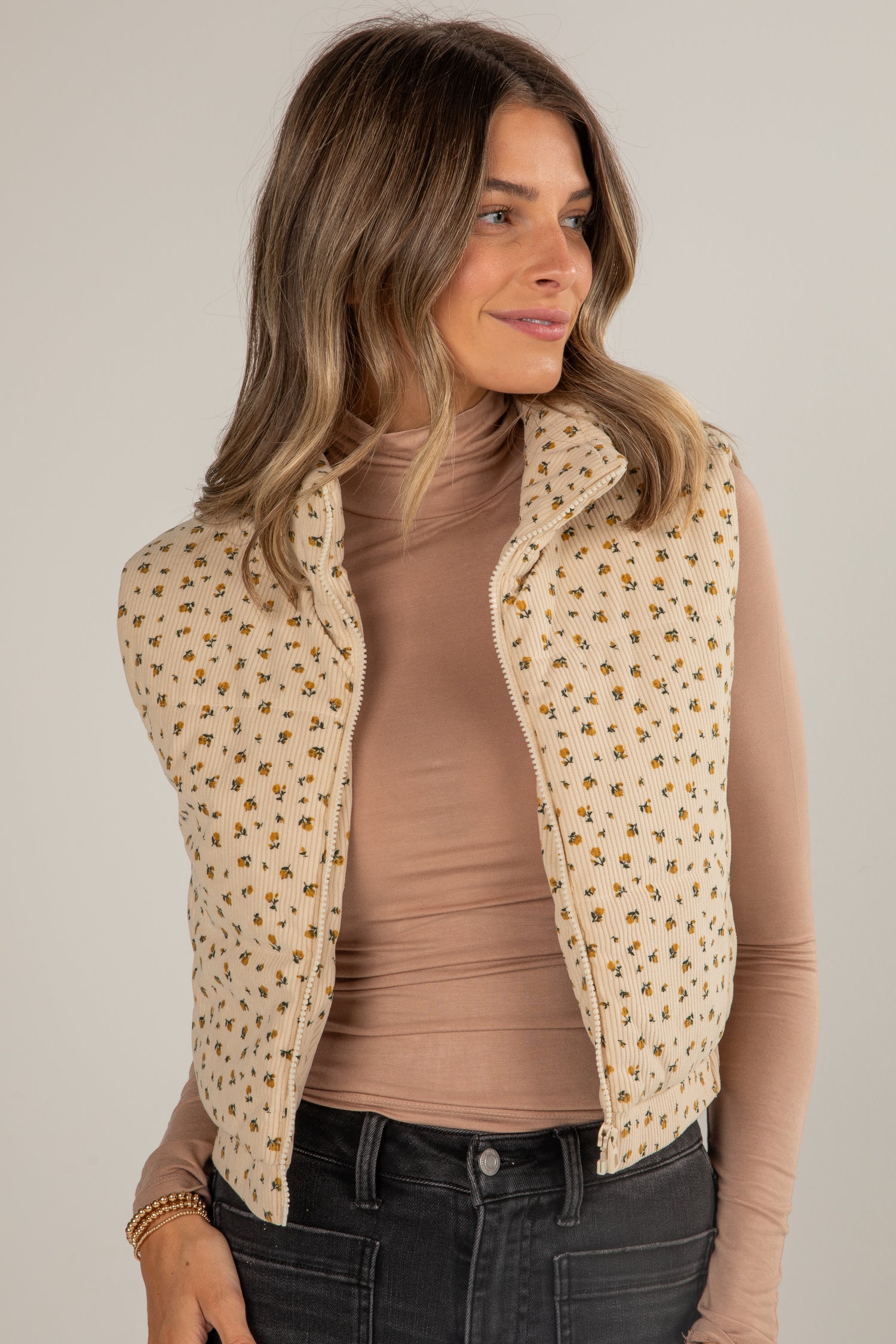Woman wearing a beige patterned vest over a brown shirt on a plain background