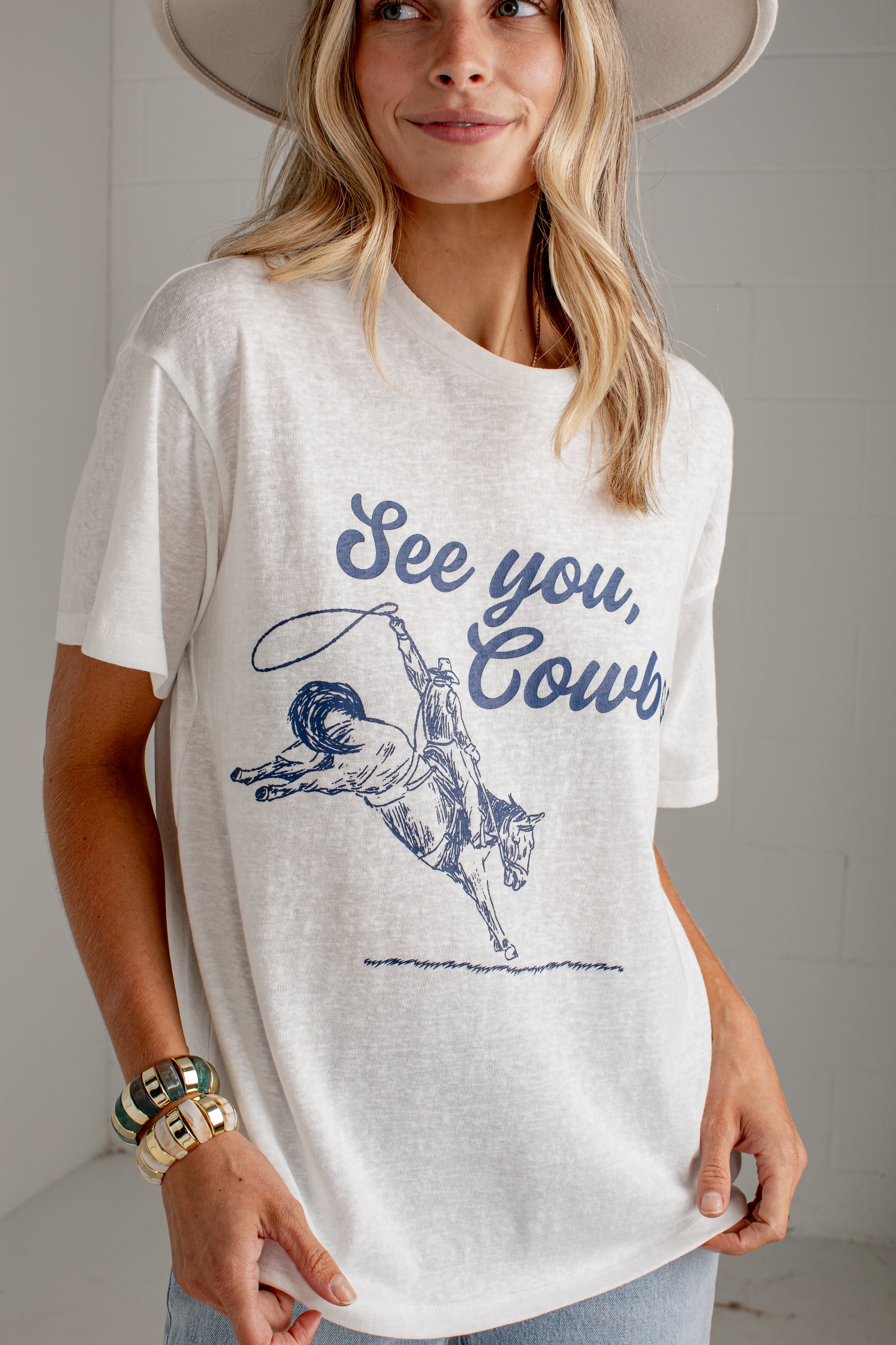A woman wearing a white graphic t-shirt with a blue cowboy design and the text &