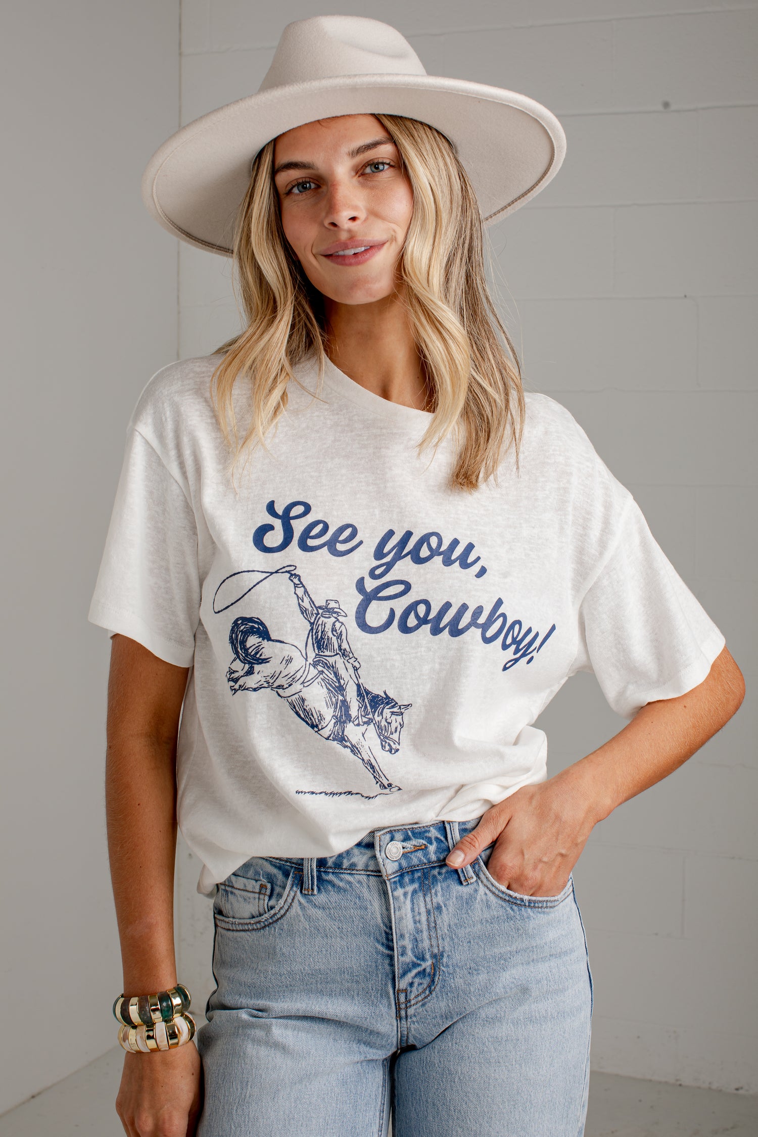A woman wearing a white graphic t-shirt with a blue cowboy design and the text &