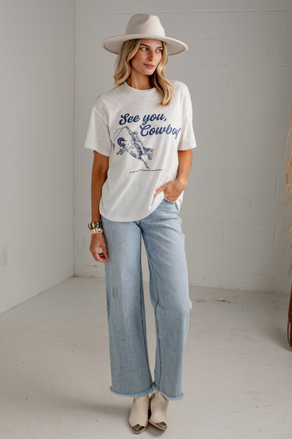 A woman wearing a white graphic t-shirt with a blue cowboy design and the text &
