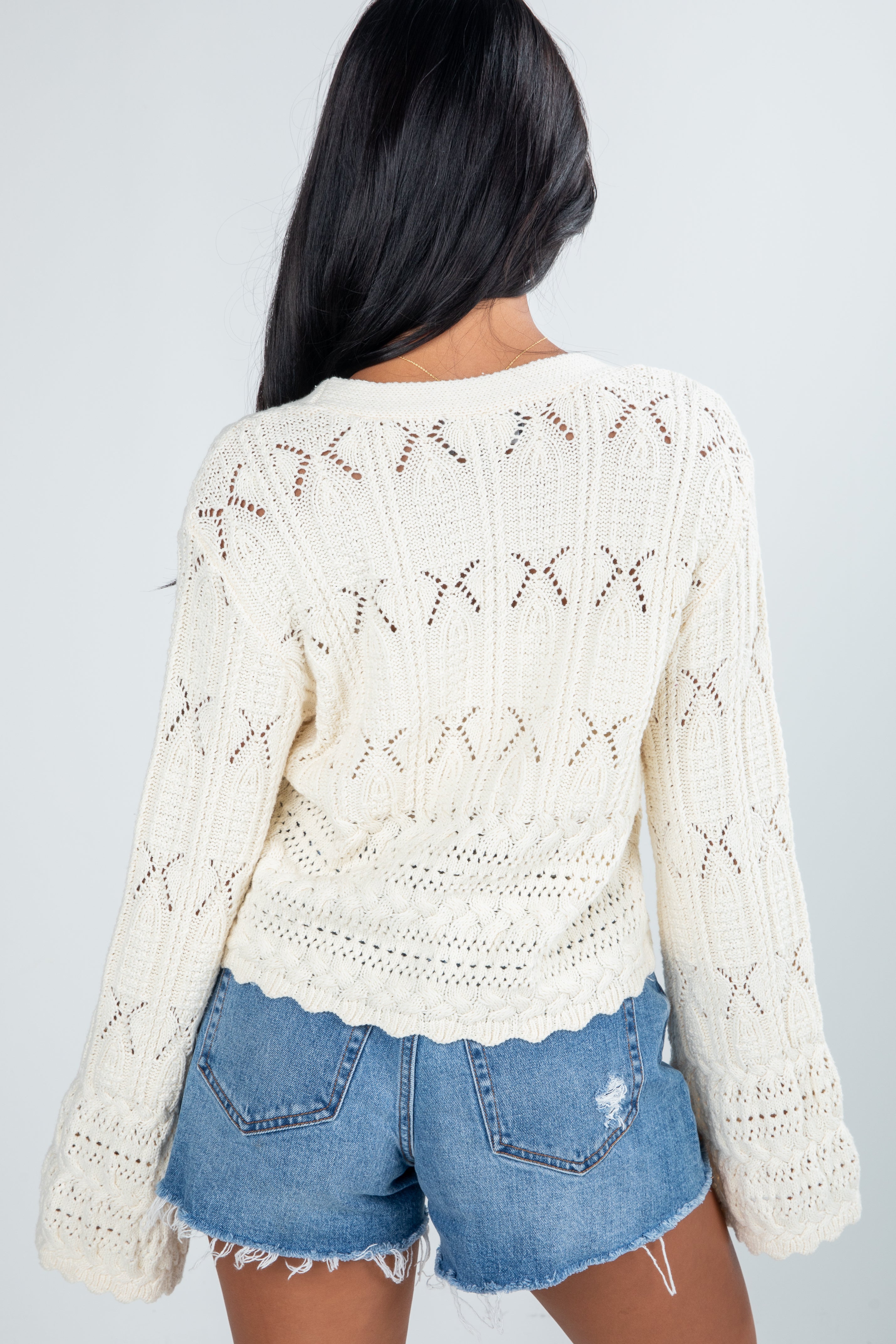 Person wearing a white lace top and denim shorts on a plain background